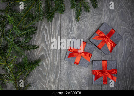 Three Christmas gifts boxes on a grey wooden floor background and the branch's of a Christmas tree bordering the left frame of photograph Stock Photo