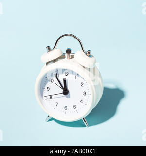 White alarm clock on blue background. Minimal styled. Stock Photo