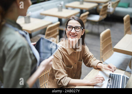 High angle portrait of young woman looking at waitress and smiling while working in cafe , copy space Stock Photo