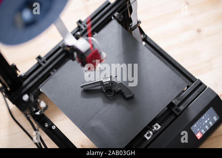 Overview of black revolver gun on working surface of 3d printer on wooden table inside modern office Stock Photo