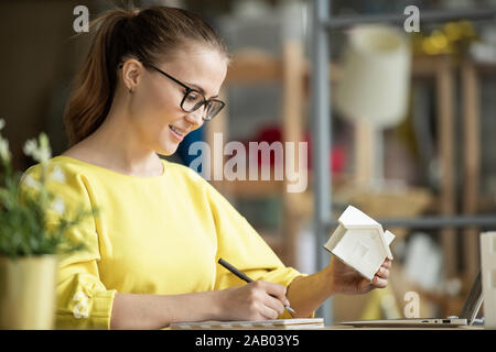 Successful young female architect with house model in hand looking through her notes while working over new project Stock Photo