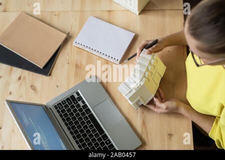 Top view of female architect describing characteristics of new residence model while sitting in front of laptop Stock Photo