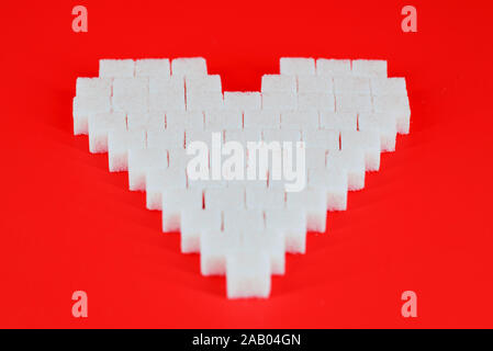 The heart made of cubes of sugar on a red background. The concept of problems associated with high blood sugar and diabetes. Sugar addiction. Stock Photo