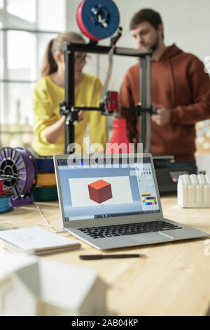 Workplace of creative designers with laptop and picture of 3d model on display and printer behind Stock Photo