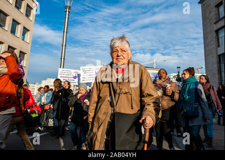 An old woman walks past a group of protesters holding placards during the demonstration.Since the beginning of 2017, there has been more than 96 femicides in Belgium, including at least 18 this year. Thousands of women and also men gathered at the Central Station in Brussels to condemn this situation but also to ask for solutions and changes in the system. Stock Photo