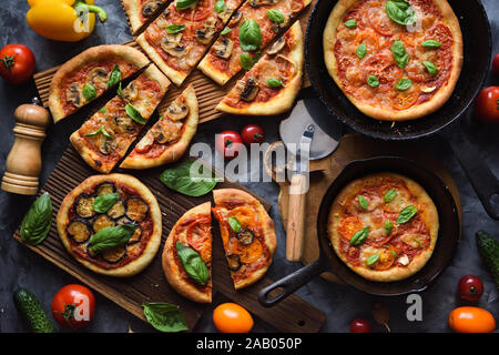 Healthy vegetarian food. Flatlay of homemade rustic pizzas with tomatoes, mushrooms, eggplants and basil with raw peppers and tomatoes in cast iron pa Stock Photo