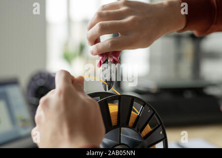 Hands of guy with nippers cutting piece of yellow filament on spool to make sample of color for 3d printing Stock Photo