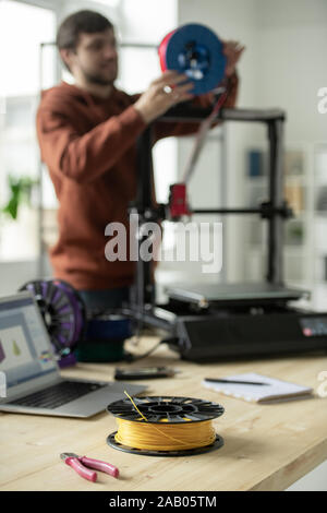 Spool with yellow filament and nippers on workplace of creative designer putting new threads in 3d printer Stock Photo