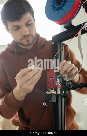 Young technician with screwdriver repairing printhead or fixing one of panels of 3d printer in office Stock Photo