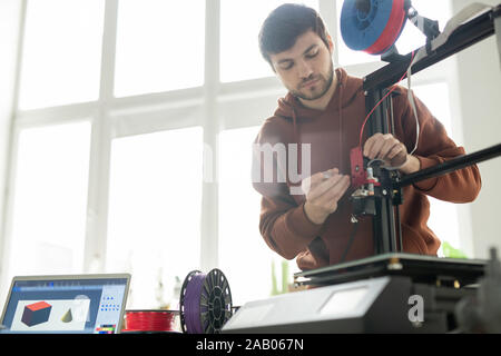 Young technician repairing or changing printhead while fixing its details on 3d printer by workplace in office Stock Photo