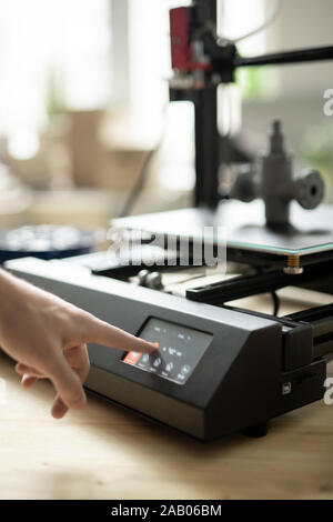 Hand of young designer pressing start button on control panel of 3d printer before beginning working process Stock Photo