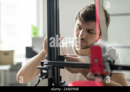 Young businessman standing in front of 3d printer while fixing some details before start of work Stock Photo