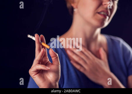 Woman smokes cigarette and has lungs or heart pain on black background. Tobacco addiction and health problem concept Stock Photo