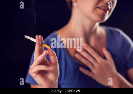 Woman smokes cigarette and has lungs or heart pain on black background. Tobacco addiction and health problem concept Stock Photo