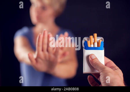 Woman in blue t-shirt refusing cigarettes on black background. Stop smoking concept Stock Photo