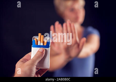 Woman in blue t-shirt refusing cigarettes on black background. Stop smoking concept Stock Photo