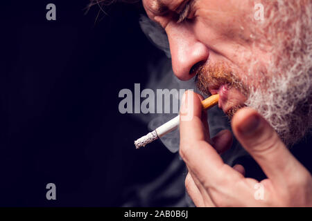 A portrait of the man smokes cigarette on black background. Tobacco addiction concept Stock Photo