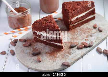 Two slices of chocolate cake, hot chocolate in a bottle, powdered cocoa and cocoa beans on a rustic table Stock Photo