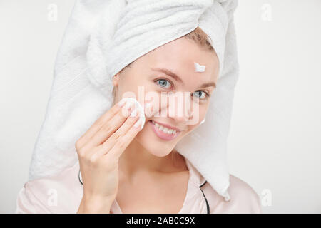 Pretty young healthy woman using cotton pad for applying hydrating cream on face Stock Photo