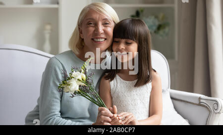 Grandmother sit on couch with little granddaughter with flowers Stock Photo