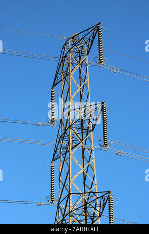 Close up of the top of an electricity pylon carrying wires for the National Grid seen against a clear blue sky on a sunny day. Stock Photo