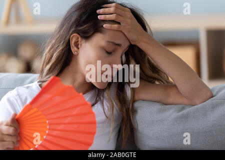 Close up woman sitting on couch reducing heat using fan Stock Photo