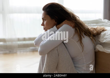 Sad woman sitting on floor leaned on bed feels lonely Stock Photo