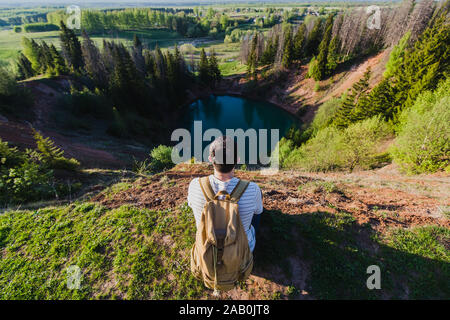 Young man tourist with backpack standing on the edge of beautiful canyon and victoriously raised hands. Male hiker reaching up top of mountain and Stock Photo