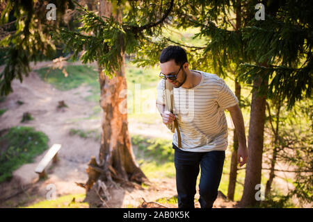 Happy bearded man traveler with backpack walking in forest. Tourism, travel, adventure, hike concept - smiling young man walking with backpack in Stock Photo
