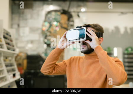 Bearded young man wearing vr headset inside contemporary optics shop Stock Photo