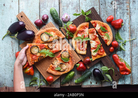 Healthy vegetarian food. Pizzas with eggplants, tomatoes and bell peppers on oak boards served with raw vegetables on shabby blue background above vie