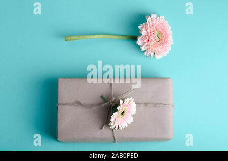 Beautiful gift boxes wrapped in simple brown kraft paper decorated with live flowers of gerbera on a gentle pastel background. Spring festive romantic Stock Photo