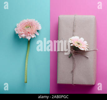 Beautiful gift boxes wrapped in simple brown kraft paper decorated with live flowers of gerbera on a gentle pastel background. Spring festive romantic Stock Photo