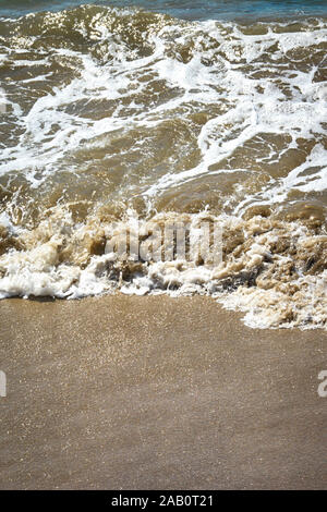 Close up view of brown colored water making small waves crashing on the beach with coarse sandy texture Stock Photo