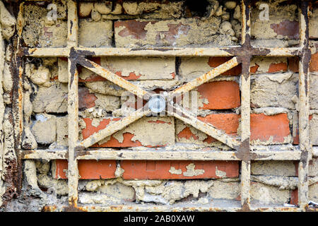 Basement bricked up and latticed window of old brick house. Part of antique painted red brick wall with walled up basement window with vintage cast ir Stock Photo