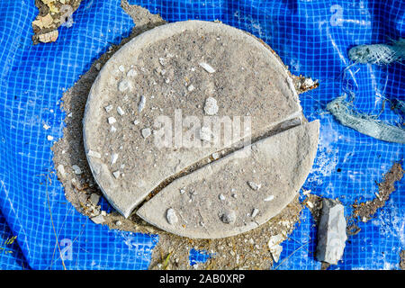 Cracked cement disc on blue reinforced checkered PVC material in shards, sand and debris. Round brocken cement detail in garbage Stock Photo