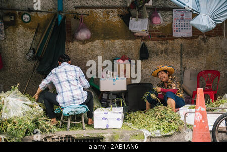 Old woman in Bangkok works on the street sorting vegtables Stock Photo