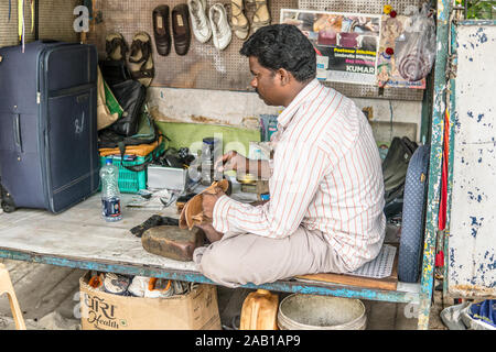 Bangalore, India, June 2018, streets of Bengaluru city, Hindu Indian shoemaker in street workshop repairing shoes and other leather items like bags Stock Photo