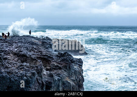 Wave crashing over person standing on rocks Stock Photo