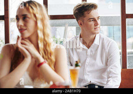 Pensive handsome young man looking away when sitting at cafe table with girlfriend Stock Photo