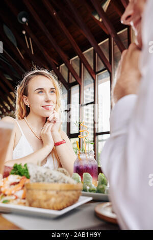 Lovely young smiling woman sitting at cafe table and enjoying dinner with her boyfriend Stock Photo