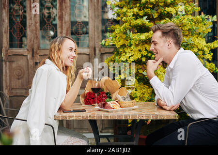Happy young couple flirting, drinking wine and eating snacks at restaurant table Stock Photo