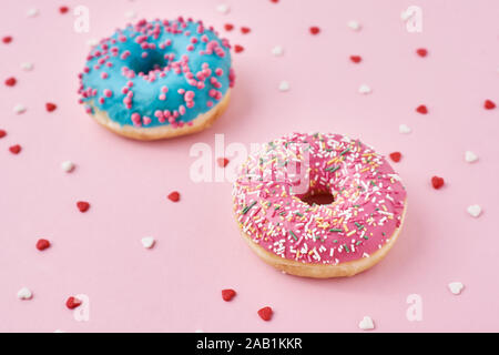 Two donuts decorated icing and sprinkles and confetti in shape of heart on pink background Stock Photo
