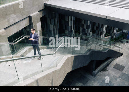 Handsome young Asian man standing on stairs and using mobile app when trying to figure out where to go Stock Photo