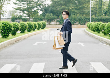 Serious confident entrepreneur with cup of coffee and shopping bags crossing road Stock Photo