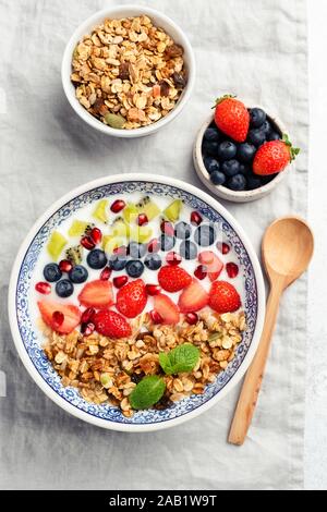 Yogurt bowl with berries, granola and fruit on linen textile backround. Table top view. Healthy vegetarian food, clean eating concept Stock Photo