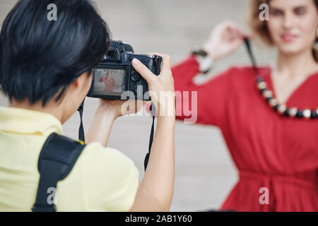 Female photographer using digital camera when shooting attractive young woman with massive necklace outdoors Stock Photo