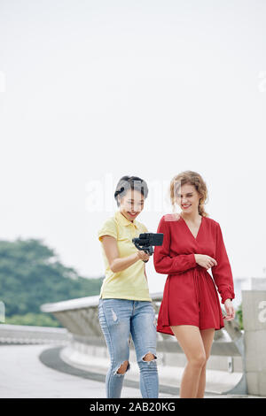 Smiling young multi-ethnic women walking outdoors and watching video they filmed together for blog Stock Photo