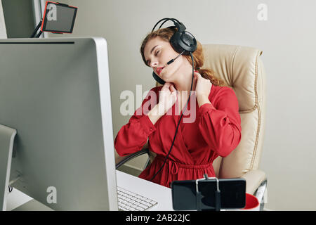 Young female editor suffering from pain in her neck after working on video for blog channel all day long Stock Photo