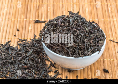 Dried tea is poured into a ceramic cup on a bamboo mat Stock Photo